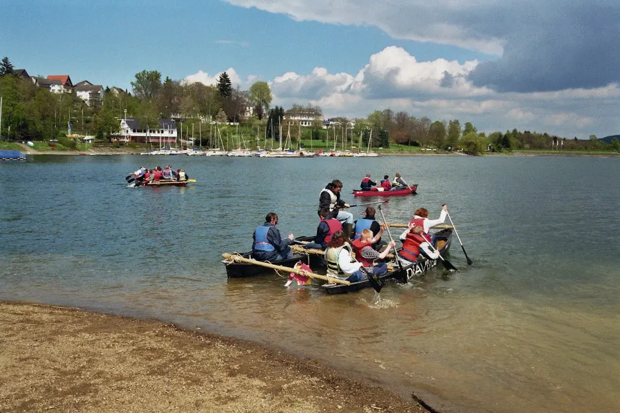 Jugendliche mit Schwimmwesten paddeln auf einem selbstgebauten Floß über den Sorpesee