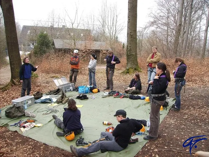 Trainerausbildung im Wald: Eine Gruppe mit Klettergurten steht um eine Plane mit Material