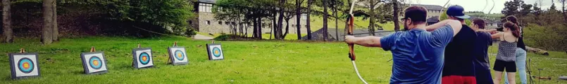 Teilnehmende schießen auf einer Wiese mit Pfeil und Bogen auf eine Reihe von Zielscheiben