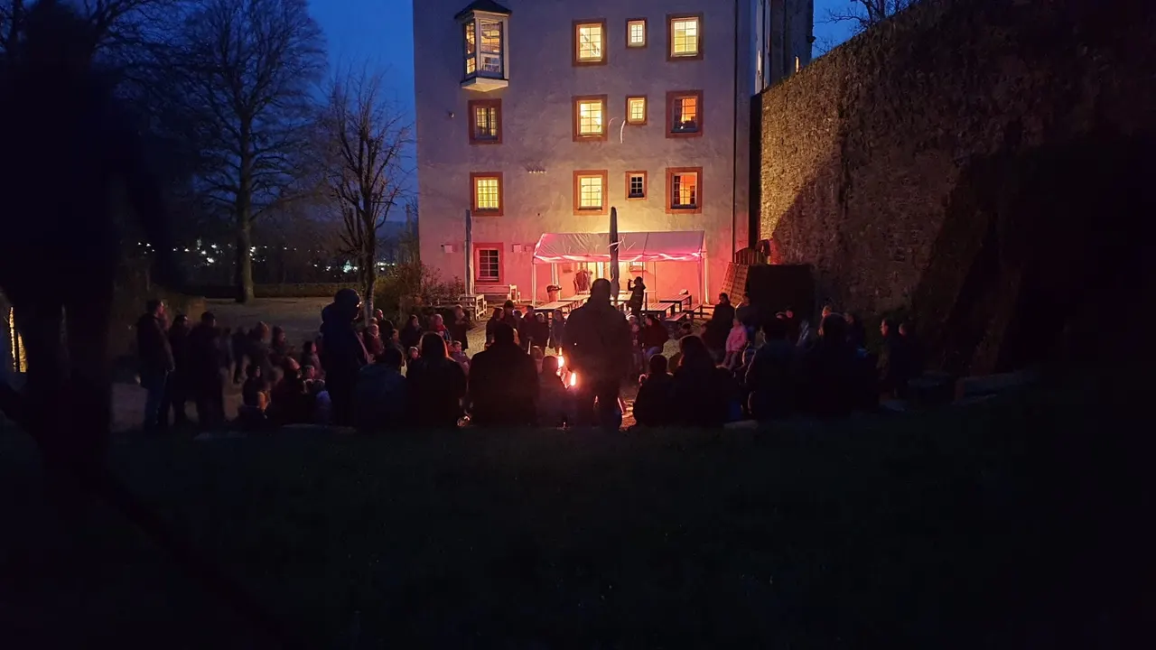 Familien sitzen am Abend um das Osterfeuer vor der hell erleuchteten Freusburg