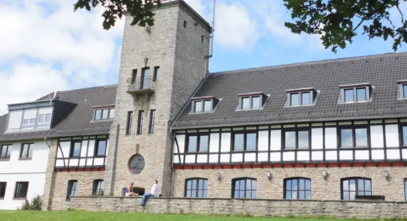 Jugendhof Finkenberg in Blankenheim: Bruchsteinturm und langes Fachwerkhaus mit Gauben, auf der Mauer davor sitzen zwei Personen