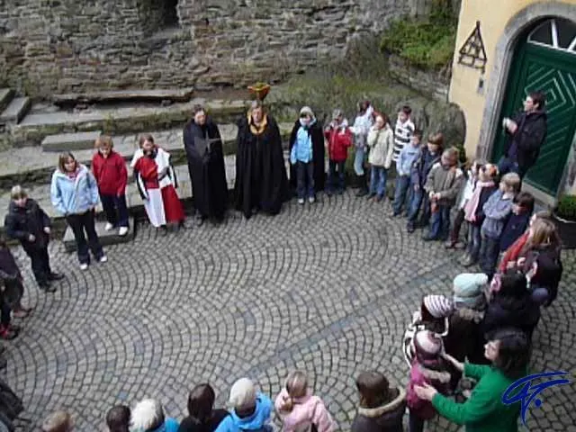 Eine Schulklasse steht im Kreis auf einem gepflasterten Burghof, in der Mitte Darsteller in mittelalterlichen Gewändern