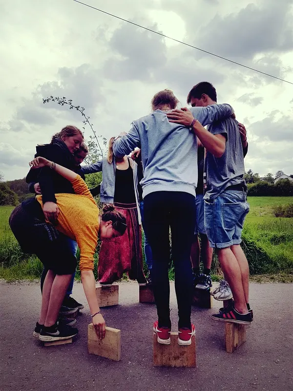 Jugendliche stehen auf kleinen Holzklötzen und halten sich gegenseitig fest