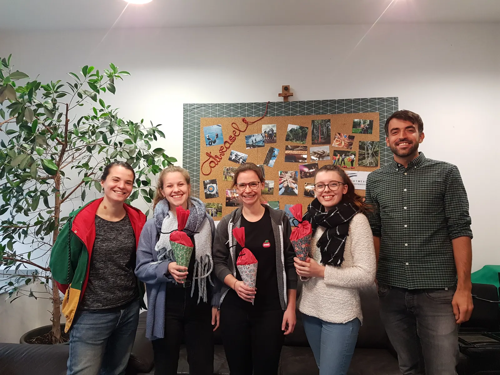 Die drei neuen Praktikantinnen mit Schultüten, eingerahmt von zwei Teammitgliedern, vor der Catweasel-Fotowand im Büro