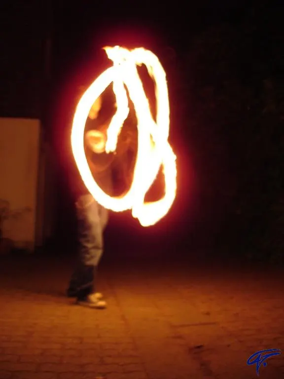 Leuchtende Feuerkreise in der Dunkelheit: Jemand schwingt brennende Feuerpois