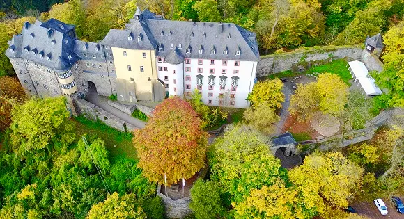 Luftaufnahme der Burg Freusburg mit Schieferdächern, Türmen und Burgmauern inmitten von herbstlich gefärbtem Wald