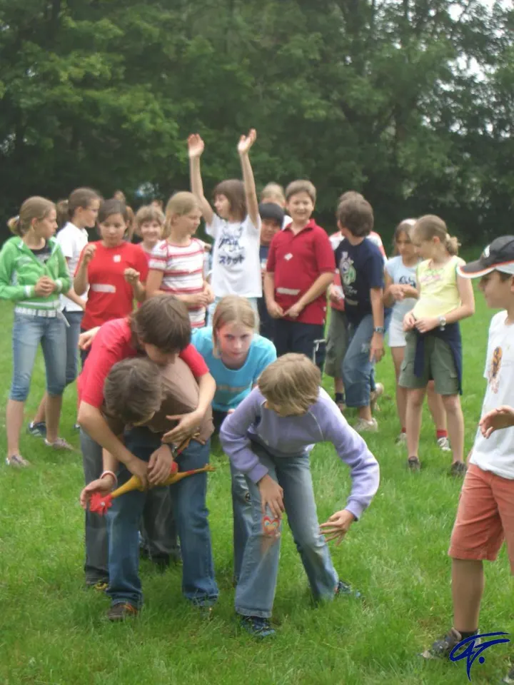Bewegungsspiel auf einer Wiese: Ein Junge hält ein Gummihuhn fest, ein Mädchen versucht es zu erwischen, die anderen Kinder schauen gespannt zu