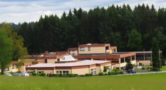 Käte-Strobel-Haus in Lieberhausen: weitläufiger, flacher Gebäudekomplex vor dunklem Nadelwald, davor eine Wiese
