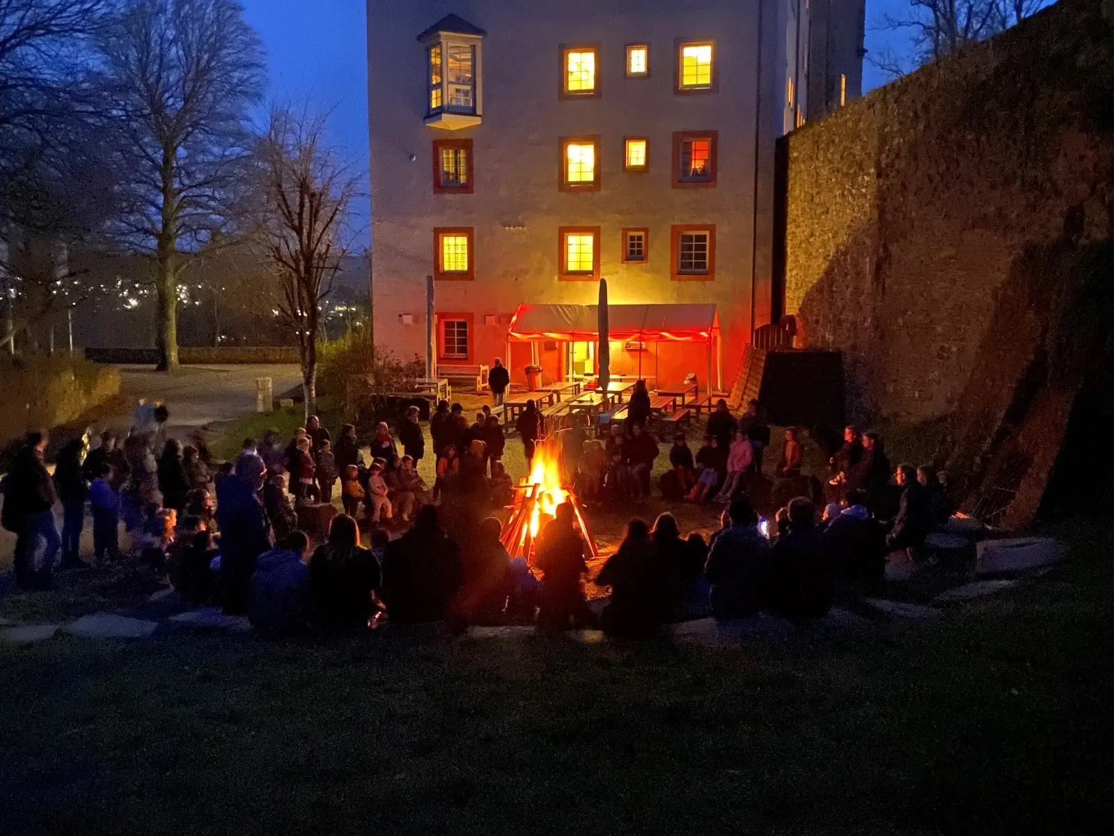 Osterfeuer am Abend im Hof der Freusburg: Familien sitzen im Kreis um das Feuer, dahinter das beleuchtete Burggebäude