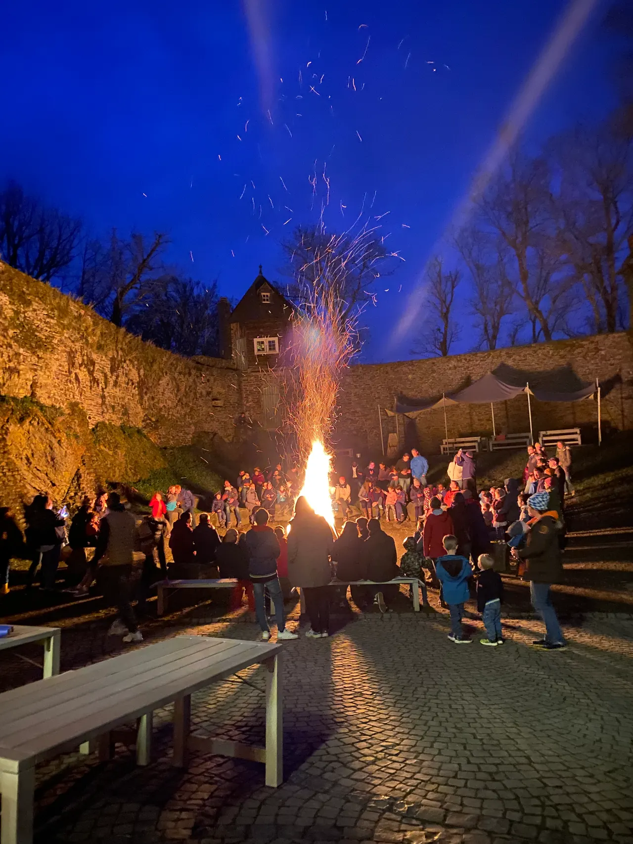 Großes Osterfeuer im Burghof der Freusburg: Funken stieben in den blauen Abendhimmel, ringsum stehen und sitzen Kinder und Eltern