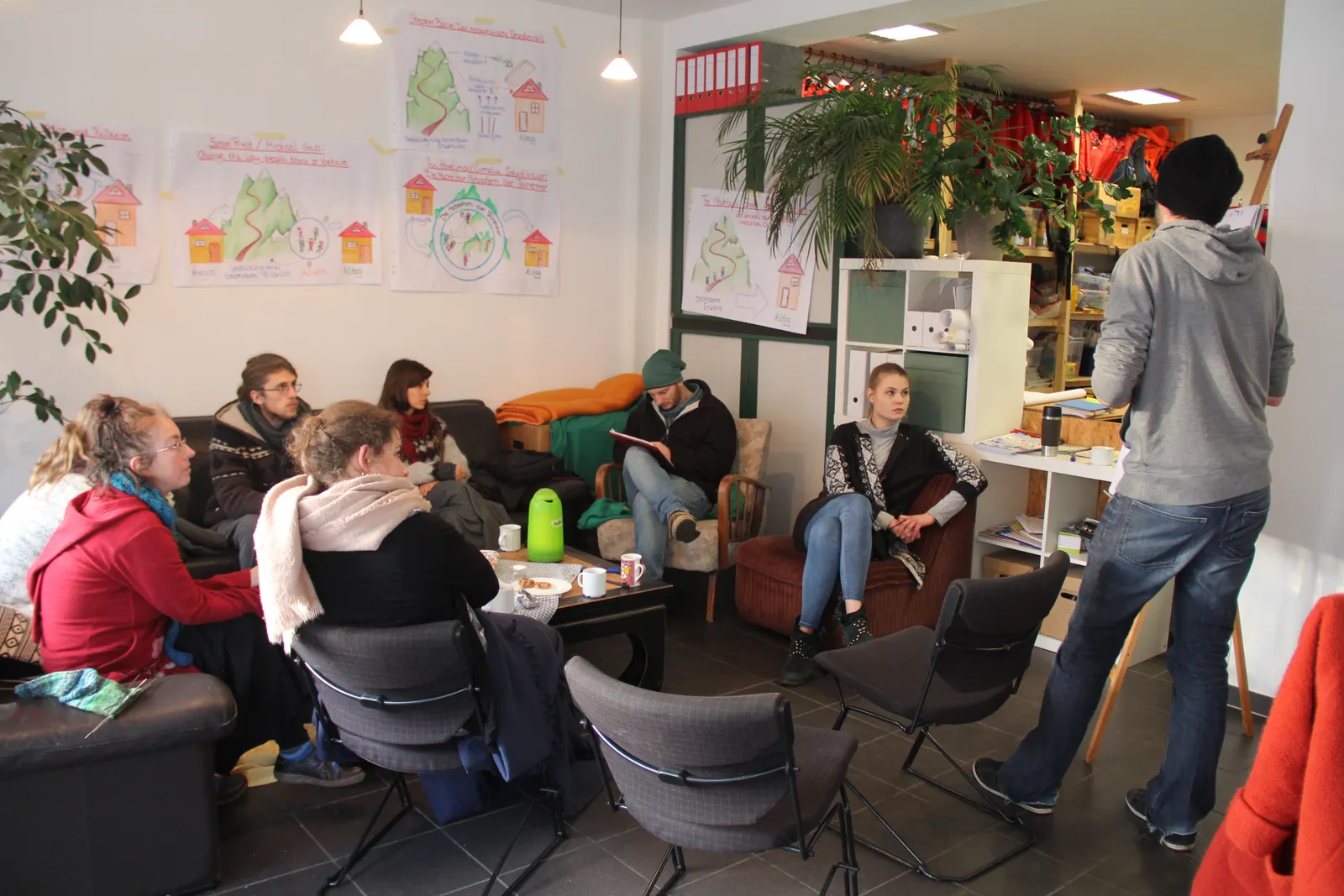 TrainerInnen sitzen bei der internen Fortbildung im Catweasel-Büro im Kreis, ein Referent steht an den Flipchart-Plakaten