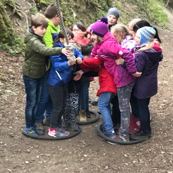 Kinder halten sich an einem Seil fest und stehen eng zusammengedrängt auf Reifen am Waldboden