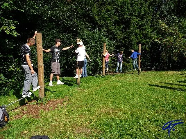 Teilnehmende balancieren auf einer Wiese über Seile, die zwischen Holzpfosten gespannt sind