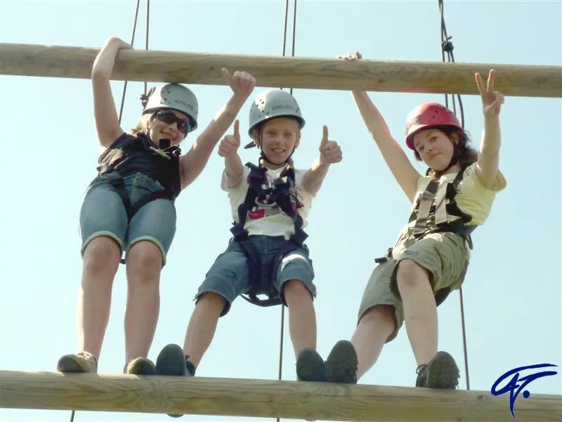 Drei Kinder mit Helmen und Klettergurten stehen gemeinsam auf einer Sprosse der Riesenleiter und strecken die Daumen hoch
