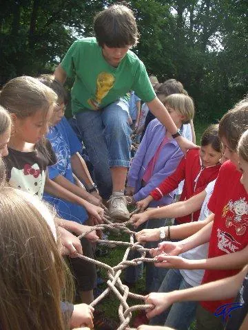 Ein Junge geht über einen Seilsteg, den die Kinder links und rechts mit ihren Händen halten