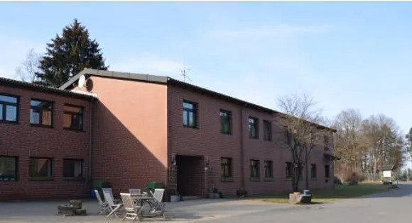Gut Ommeroth: zweigeschossiges Backsteingebäude mit Gartenstühlen auf dem Vorplatz unter blauem Himmel