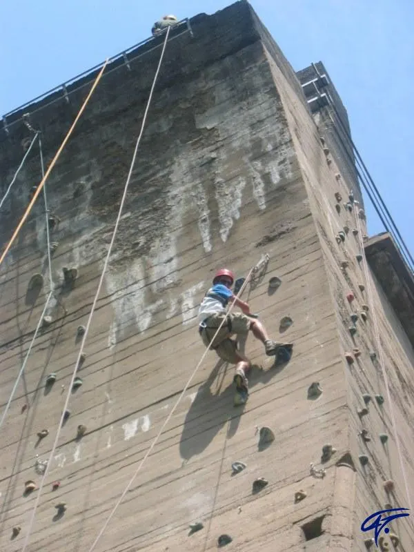 Ein Kind klettert gesichert an einem hohen Betonpfeiler mit Klettergriffen