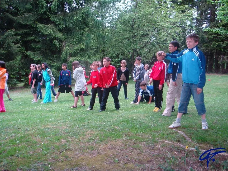 Kinder stehen bei einem Bewegungsspiel auf einer Wiese vor hohen Tannen